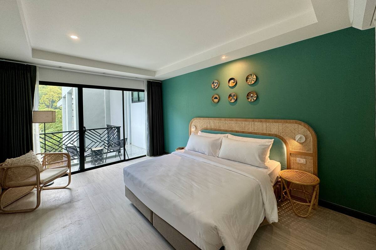 A modern hotel room with a large bed, a balcony with a view, and a green accent wall.