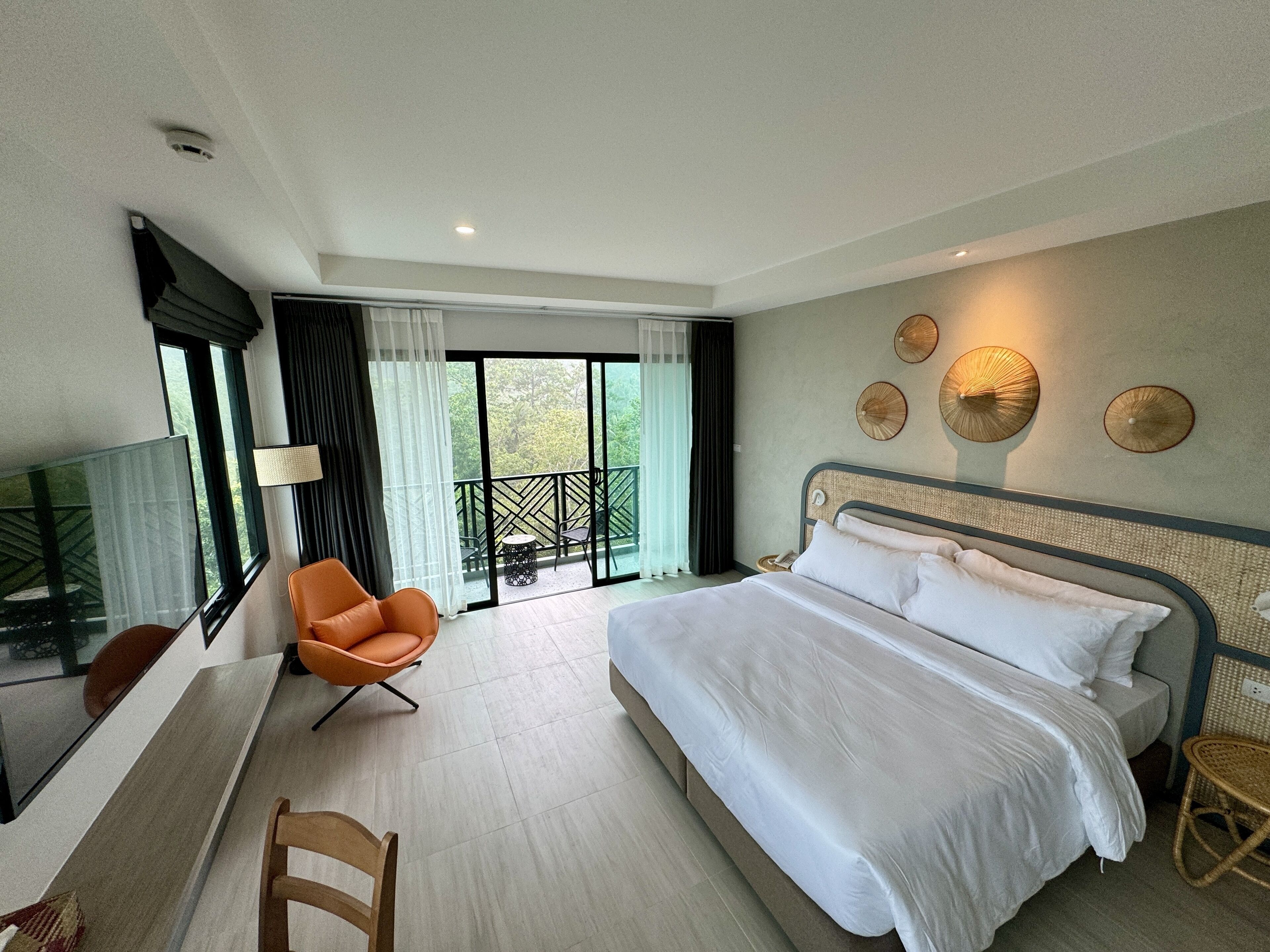 Habitación de hotel con una cama grande, un escritorio, una silla, un balcón con mesa y sillas, y detalles decorativos en las paredes.