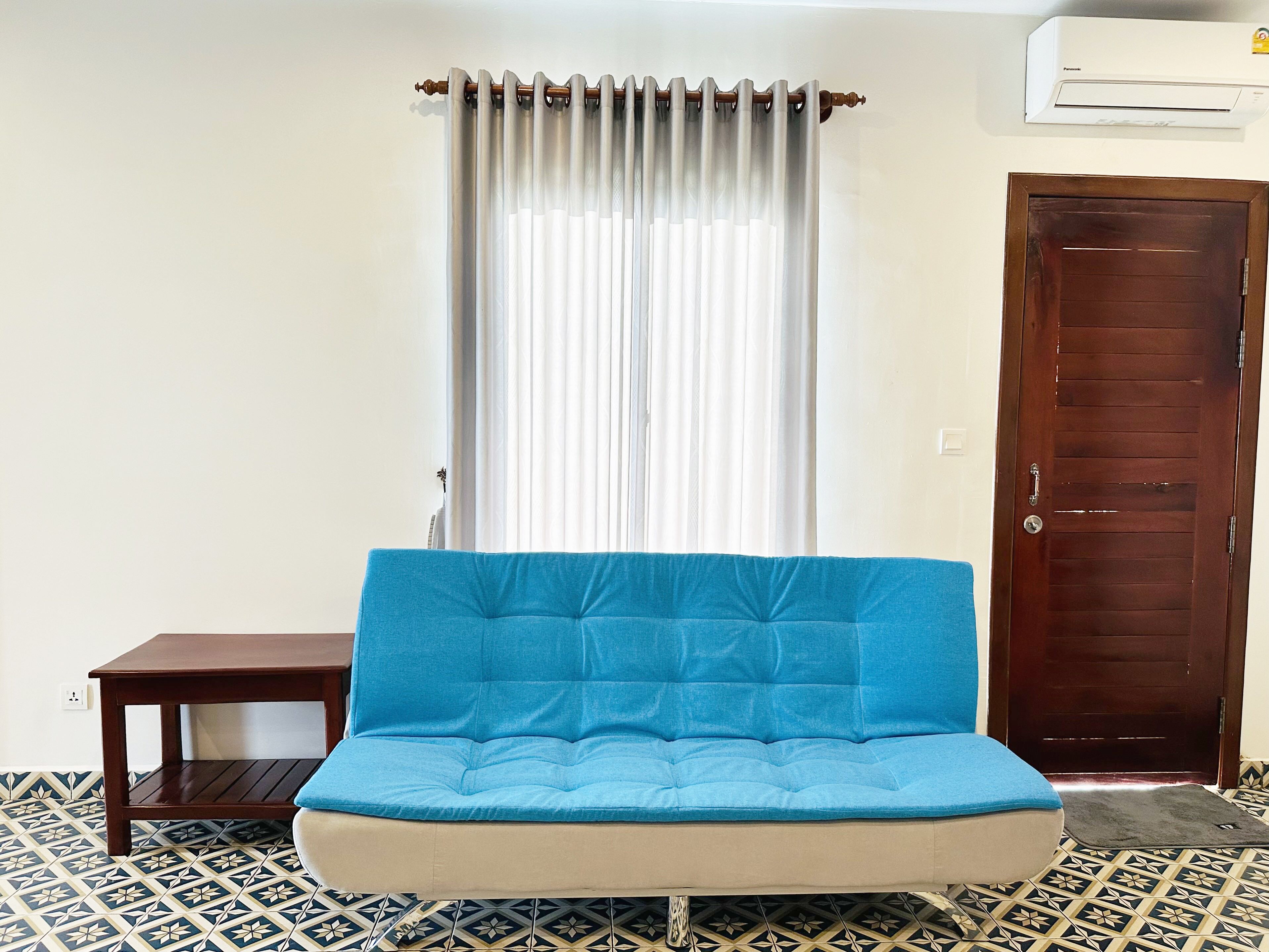 A room with a blue sofa, a small wooden table, a patterned floor, a white curtain, and a wooden door.
