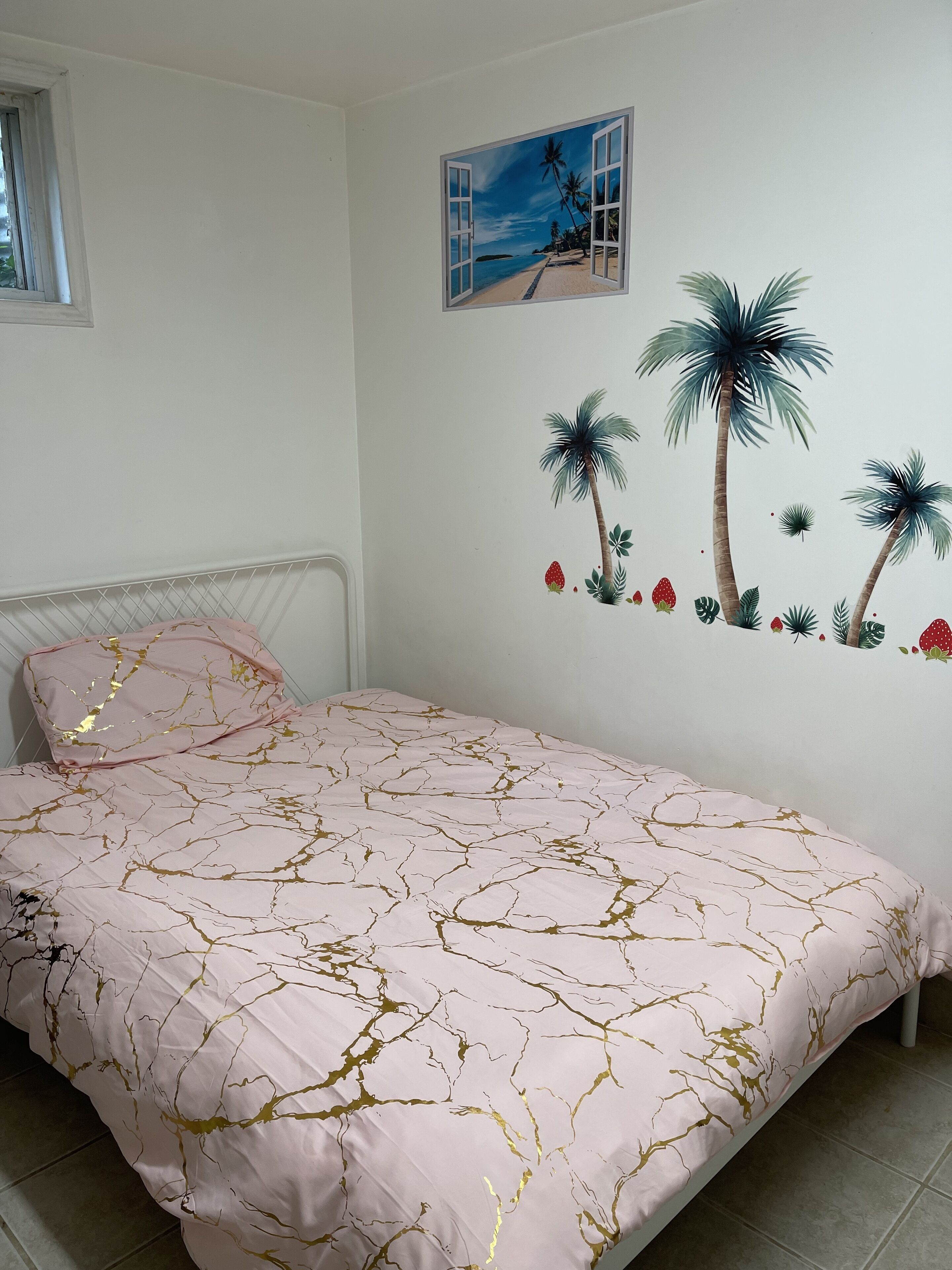 Une chambre à coucher avec un lit, une fenêtre et une fresque murale représentant des palmiers et des fraises.