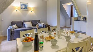A dining area with a table set for breakfast, a sofa in the background, and a kitchen visible through an open door.