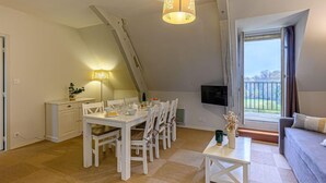 A dining area with a table set for four, a TV mounted on the wall, and a balcony with a view.