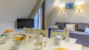 A dining area with a table set for breakfast, a sofa, and a TV in the background.