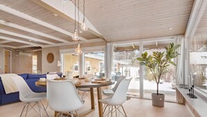 A modern dining area with a wooden table, white chairs, and a large window with a view of a snowy landscape.