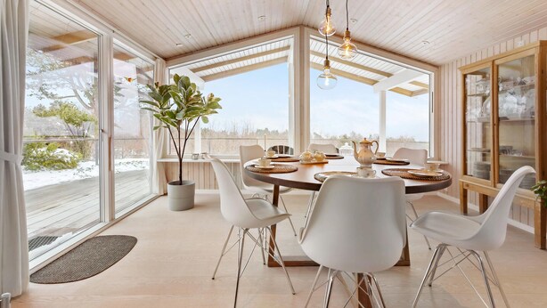 A modern dining area with a round table, white chairs, and a large window offering a view of the outdoors.