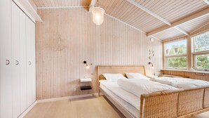 A bedroom with a wooden slatted wall, a bed with white bedding, a bedside table with a lamp, and a window with a view of greenery.