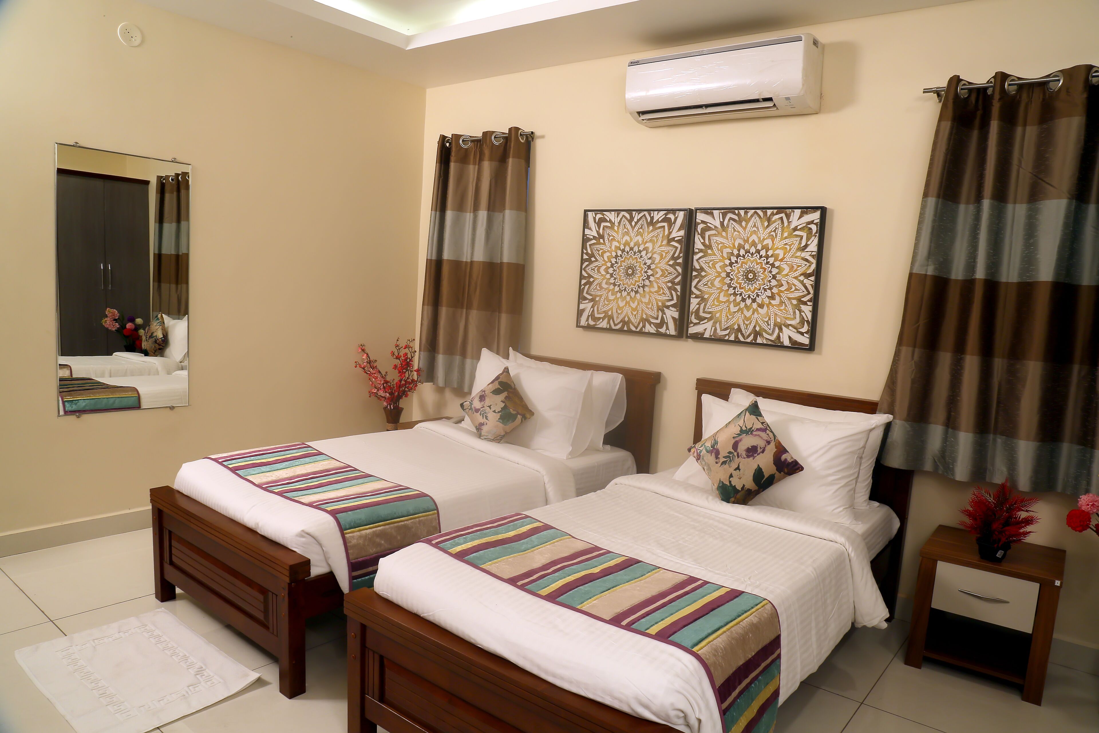 A hotel room with two beds, a mirror, an air conditioner, and decorative wall art.