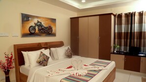 A neatly made bed with a striped bedspread, a painting of a motorcycle, a wardrobe, and a plant on the windowsill. - The Capital Executive Service Apartment (Guntur)