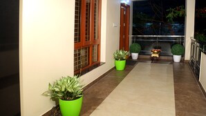 A hallway with potted plants, a wooden door, and a balcony with a railing. - The Capital Executive Service Apartment (Guntur)