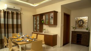 A dining area with a table set for four, surrounded by chairs, and a cabinet with glass doors. - The Capital Executive Service Apartment (Guntur)