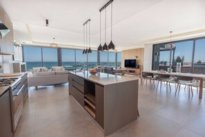 A modern kitchen with a large island, a dining area with a view, and a living space with a sofa and TV.
