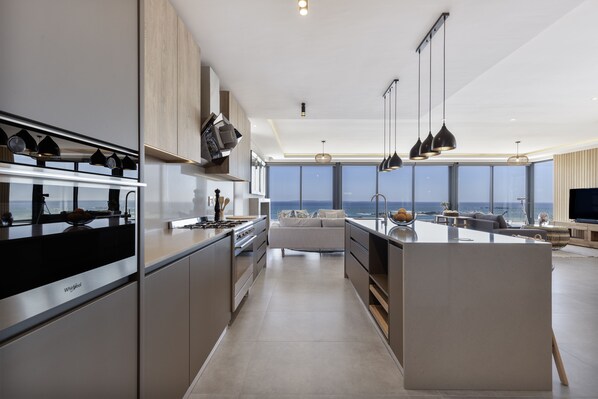 A modern kitchen with a central island, built-in appliances, and a view of the sea.