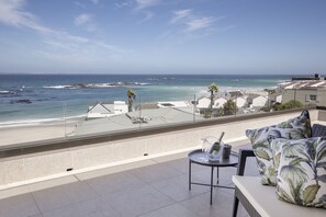 A balcony with a view of the beach, a table with a glass, and a sofa with floral cushions.