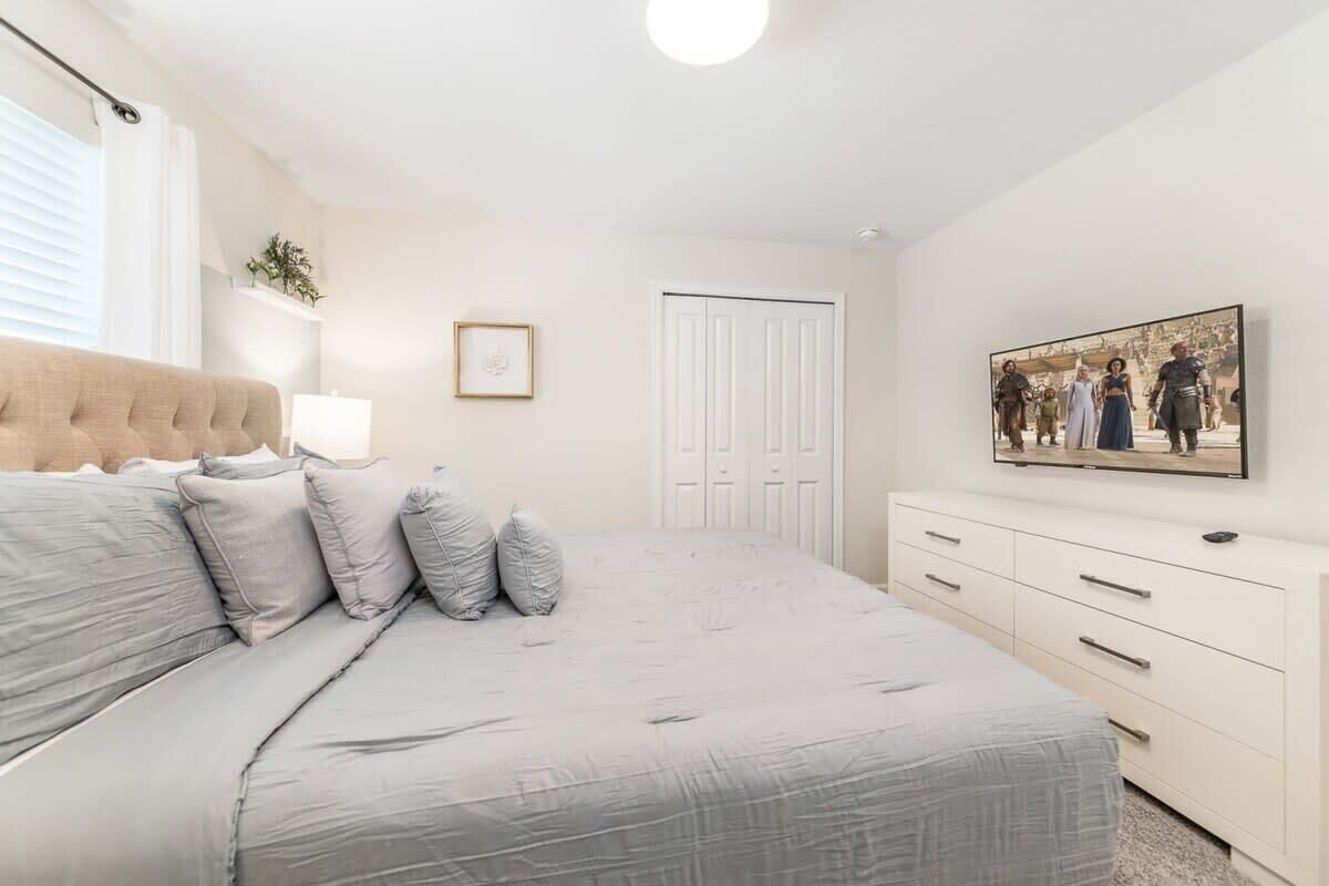 Une chambre à coucher avec un lit, une commode, un tableau encadré et une porte.