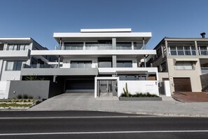 A modern multi-story residential building with a flat roof, large windows, and a gated entrance.