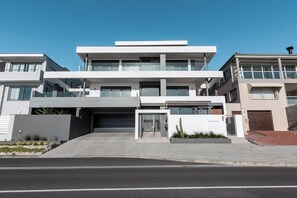 A modern multi-story residential building with a flat roof, large windows, and a gated entrance.