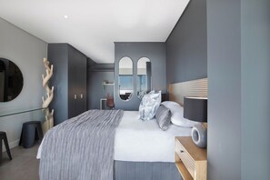 A modern bedroom with a large bed, a bedside table, a mirror, and a unique wall sculpture.