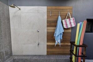 A shower area with a wooden panel wall, a hanging towel, and colorful mats.