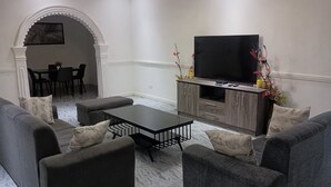 En stue med fjernsyn, sofa og spiseplads med stole og bord.