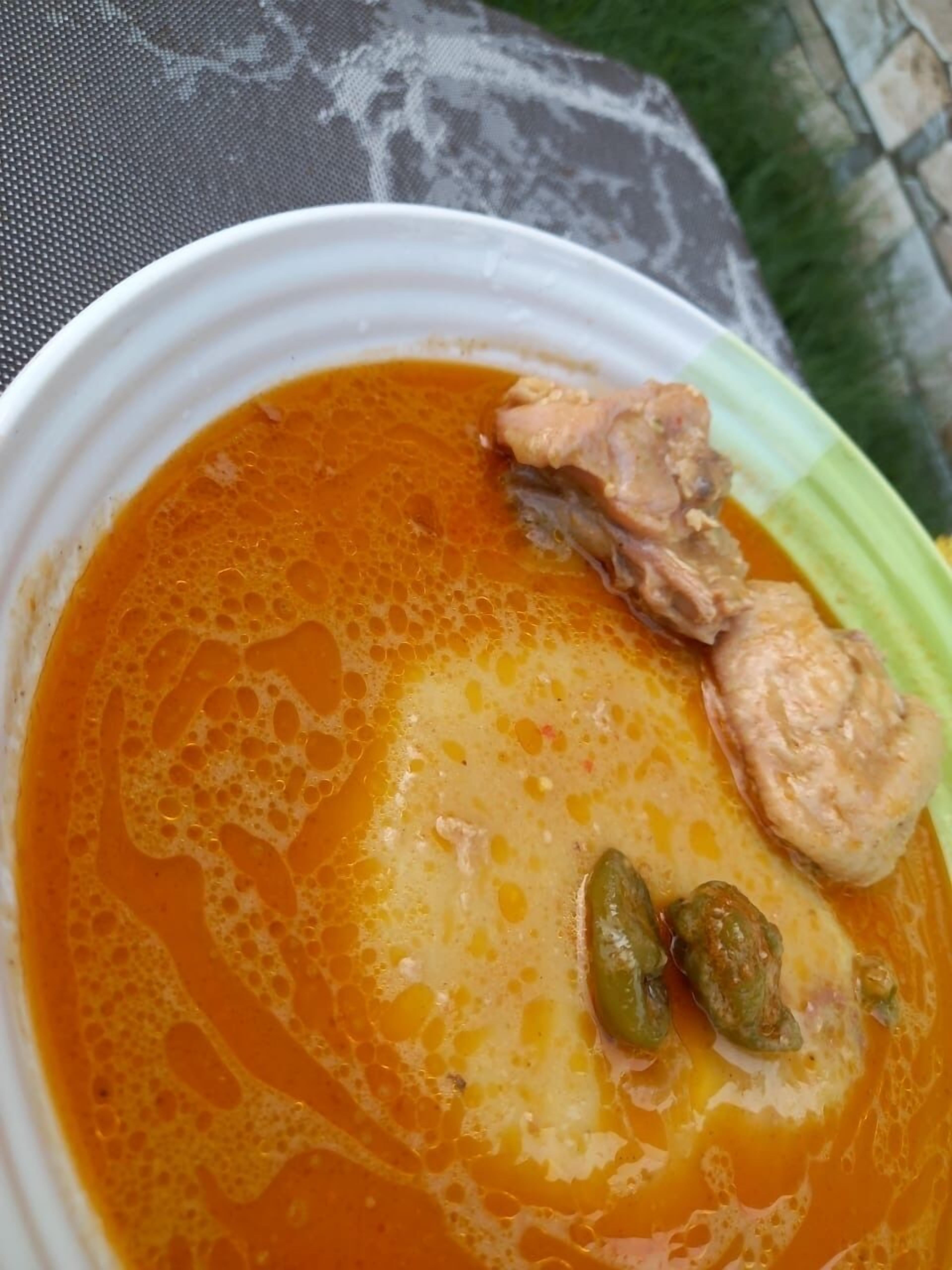 Uma tigela de sopa com caldo claro, pedaços de carne e vegetais verdes.