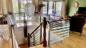 Un vaste espace de vie agrémenté d’un escalier en verre, d’un grand lustre et offrant une vue sur l’extérieur grâce à de larges fenêtres.
