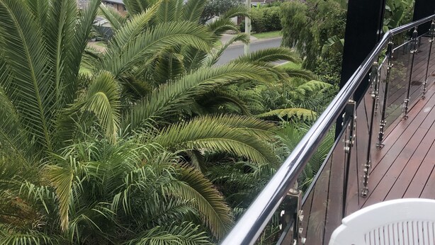 Un balcon donnant sur une route, de la verdure et une colline au loin.