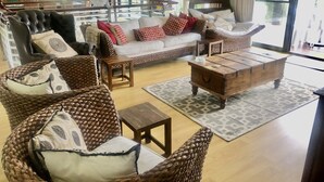 Un grand salon comprenant un canapé, deux fauteuils en osier, une table basse en bois et une petite table d’appoint.