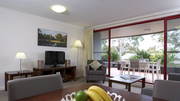 A hotel room with a dining area, a TV, a sofa, and a balcony with outdoor furniture.