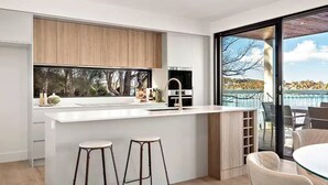 A modern kitchen with a large island, bar stools, and a view of a body of water. - Luxury Villas Clare De Lune Waterfront (with pool) (Central Coast)