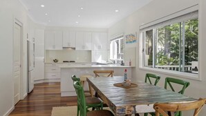 Una cocina moderna con armarios blancos, una mesa de comedor de madera con sillas verdes y un ventanal con vistas a árboles.