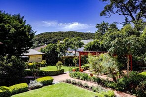Stroll through the serene garden, surrounded by lush plants and a picturesque pergola, leading to a charming building with a warm facade.