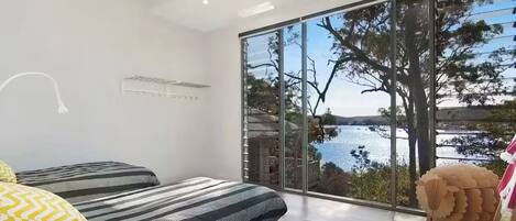 Ein modernes Schlafzimmer mit einem großen Schiebeglastür, die auf einen Balkon mit Seeblick führt.