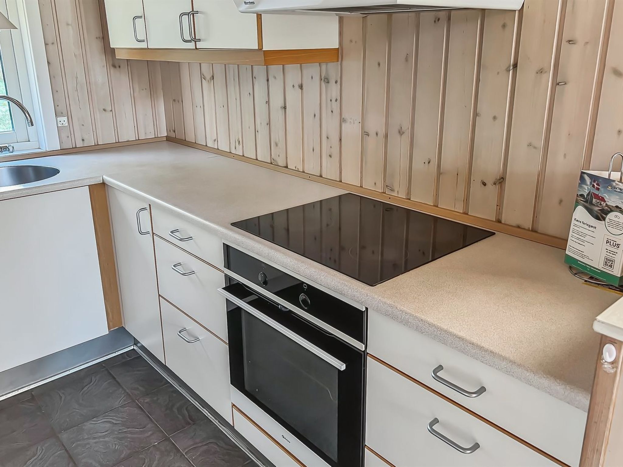 Une cuisine moderne avec des meubles blancs, une plaque de cuisson à induction noire et un four encastré.