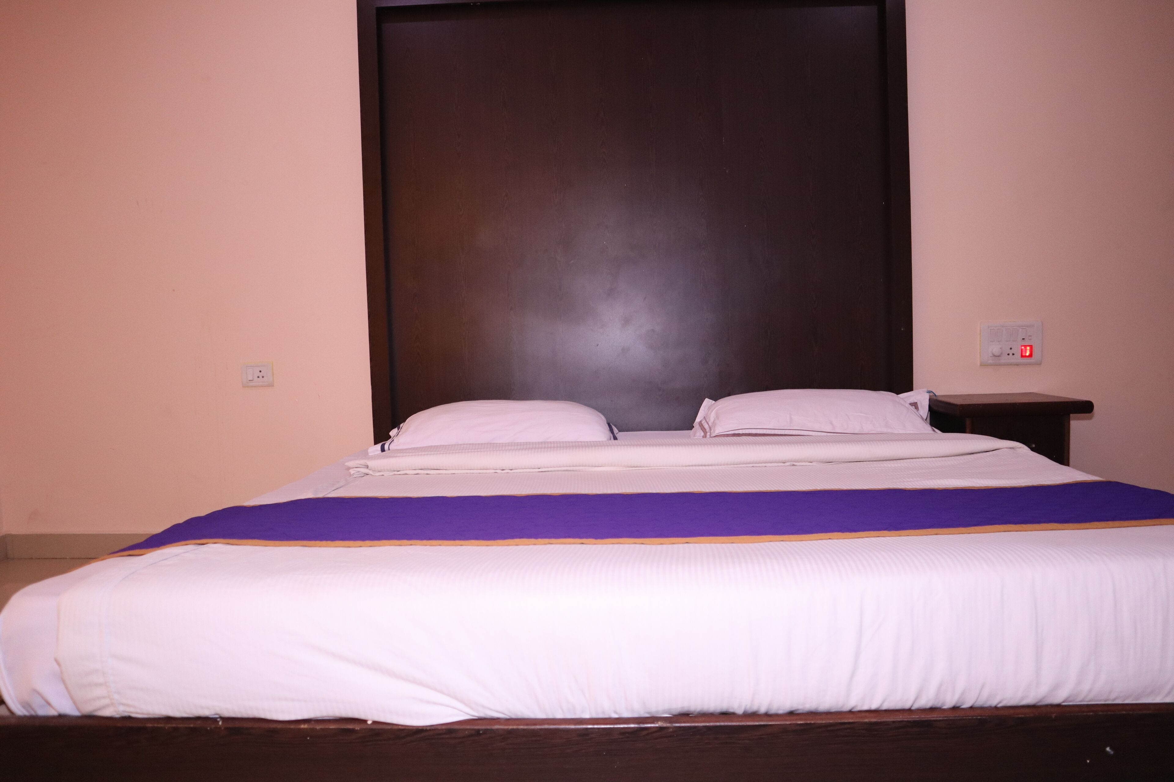 A bed with white bedding and a purple and orange accent.
