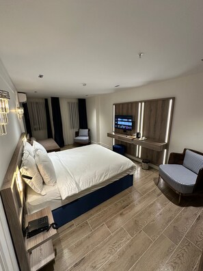 Ett modernt hotellrum med en stor säng, ett skrivbord, en stol, en tv och en minibar.