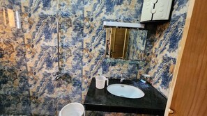 A bathroom with a marble wall, a black sink, a mirror, and a white bucket.
