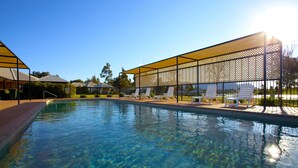 A clear swimming pool with sunlit water, surrounded by white lounge chairs and a shaded area with a metal fence. - Club Wyndham Pokolbin Hill (Pokolbin)