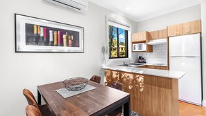 A modern kitchen with wooden cabinets, a white countertop, and a built-in microwave. There is a dining area with a wooden table and chairs, and a framed picture on the wall. - Club Wyndham Pokolbin Hill (Pokolbin)