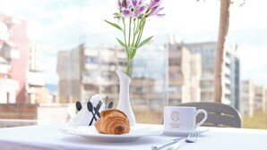 A table with a croissant, a white cup with hotel branding, and a vase with flowers.