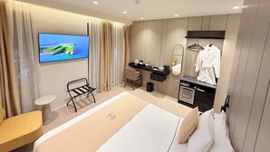 Una habitación de hotel moderna con una cama grande, un televisor montado en la pared, un escritorio pequeño con un espejo y una bata colgada en un perchero.