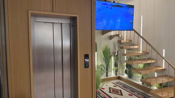 A modern interior with a wooden door, a staircase with a patterned rug, and a flat-screen TV mounted on the wall.
