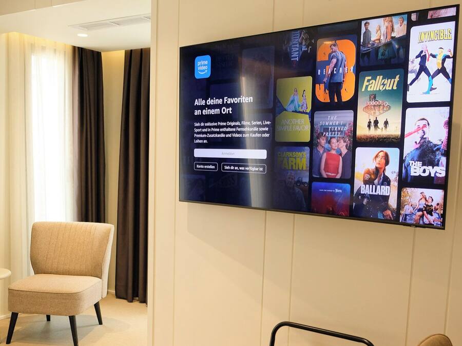 Habitación de hotel con una televisión de pantalla plana mostrando carteles de películas, una cama, una silla y una pequeña mesa.