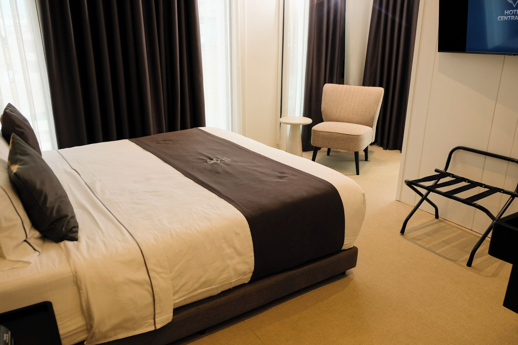 A hotel room with a bed, a chair, a TV, and a small table.