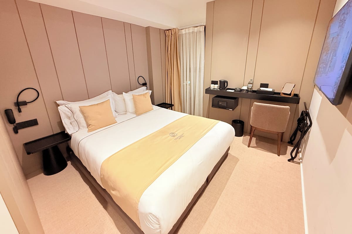 A hotel room with a bed, desk, chair, and a television.