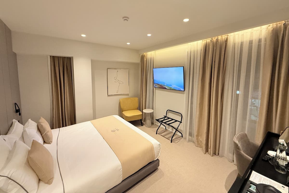 A hotel room with a large bed, a desk with a lamp, a chair, and a TV mounted on the wall.