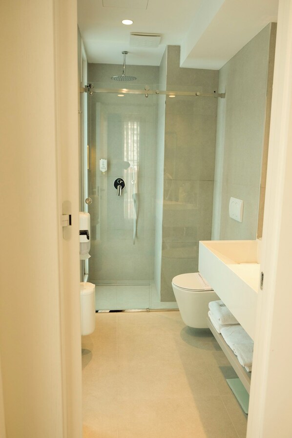 A modern bathroom with a glass-enclosed shower, a toilet, and a vanity with a towel rack.