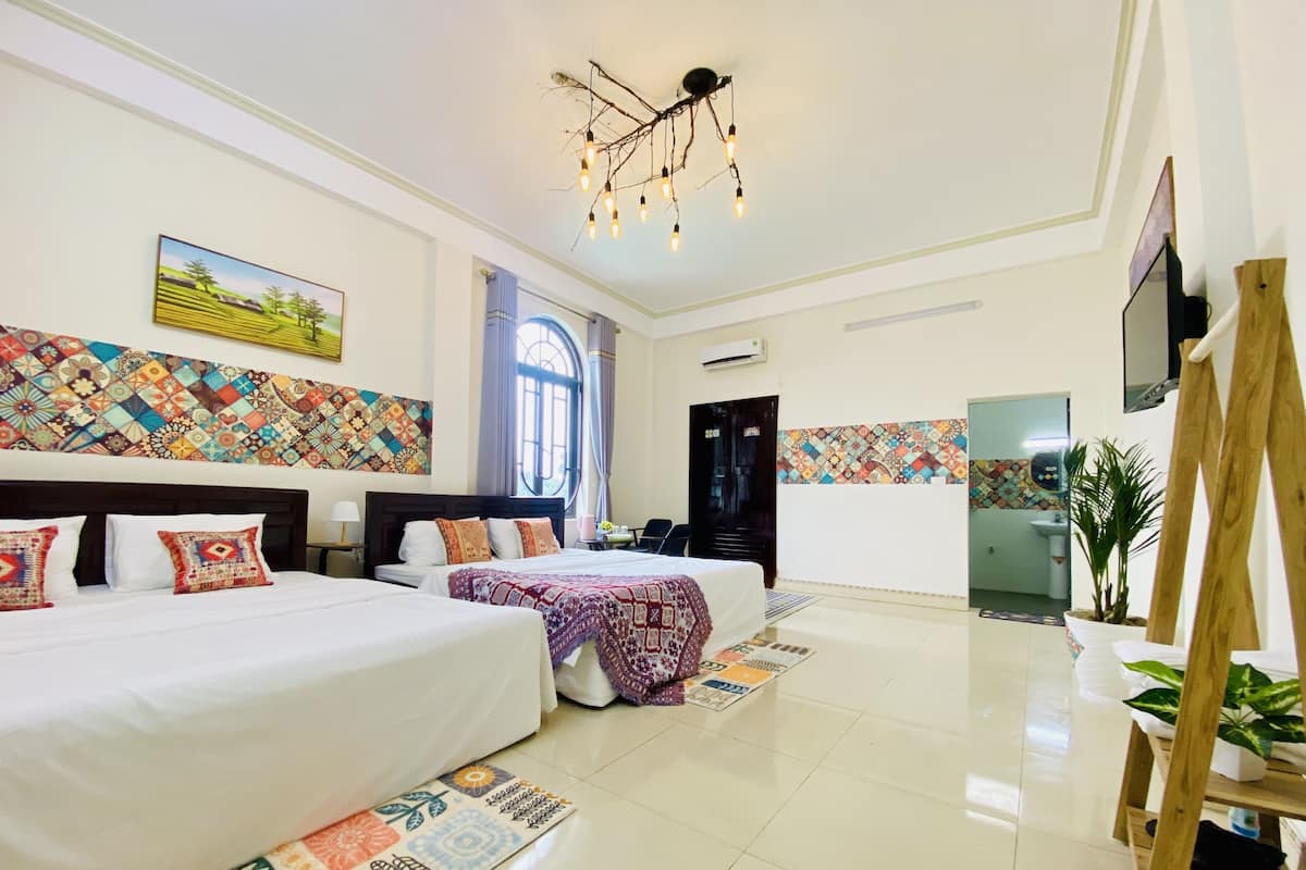 A hotel room with two beds, a large window, a ceiling light fixture, and a wall-mounted TV.