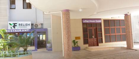A hostel entrance with a tiled roof, a sign for 'Luther House Hostel', and a 'RELIISH FOODS' restaurant in the background.