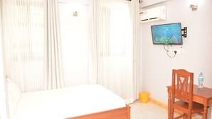 Un dormitorio con cama, cortinas, televisor, una silla de madera y una mesita.