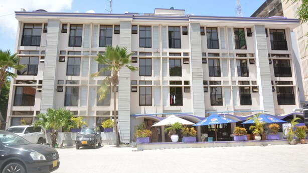 Un hotel de varios pisos con fachada moderna, balcones y mobiliario exterior con sombrillas.